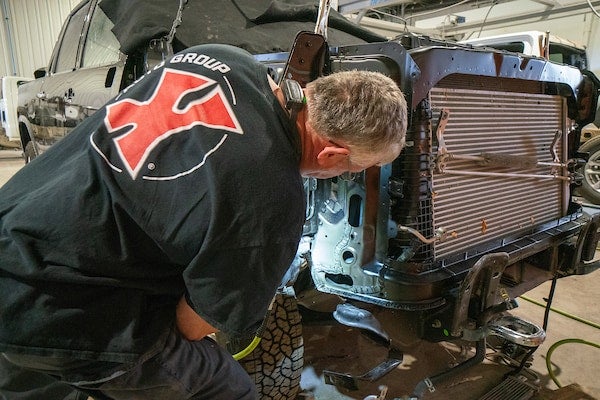 Mechanic leans into the engine bay of a partially disassembled vehicle, focusing on repairs.